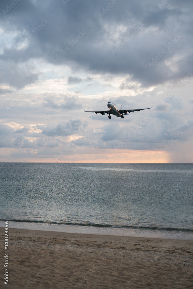 View from the sandy beach on the landing airplane isolated above the sea over beautiful cloudy sky background