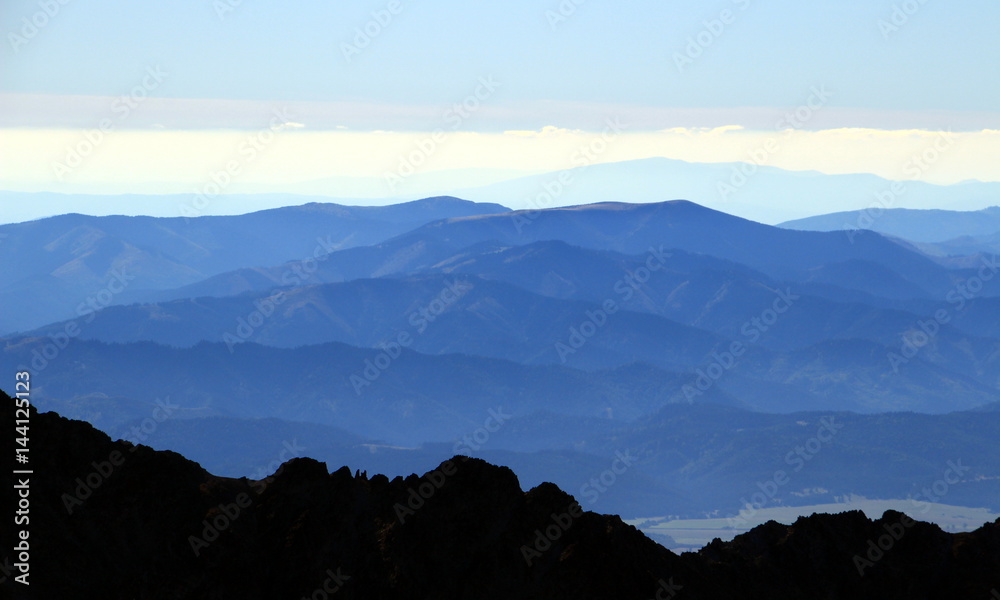 Obraz premium Blue ridges in Low Tatra National Park and Slovak Central Mountains with Velky bok and Polana peaks, from Lomnicky peak, High Tatras, Slovakia, Europe.