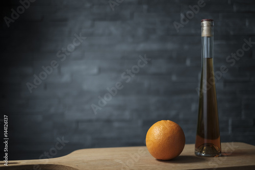 Fotografie orange with a bottle of liquor on a wooden plank
