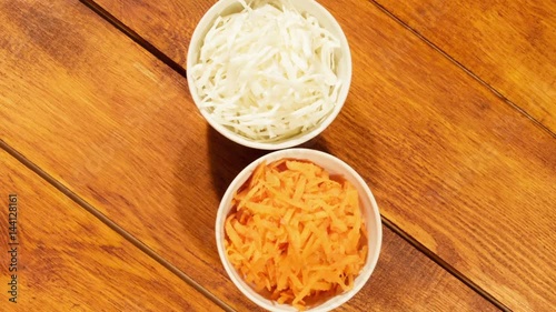 Chopped carrot and cabbage in white cup on wooden background close up. Ingredients for vegetable salad