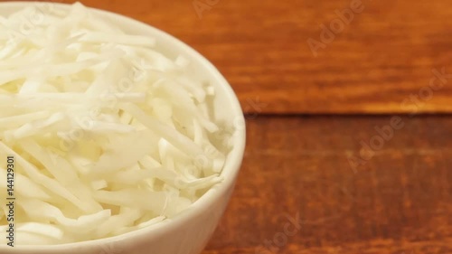 Chopped cabbage in white cup on wooden background close up. Ingredient for vegetable salad
