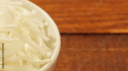 Chopped cabbage in white cup on wooden background close up. Ingredient for vegetable salad