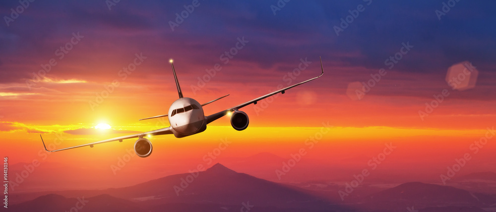 Fototapeta premium Komercyjny samolot latający nad górami w zachód słońca