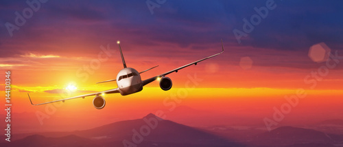 Commercial airplane flying above mountains in sunset