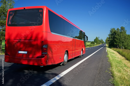 Obraz na płótnie The red bus traveling on asphalt road lined avenue of trees in a rural landscape on a bright sunny day w salonie