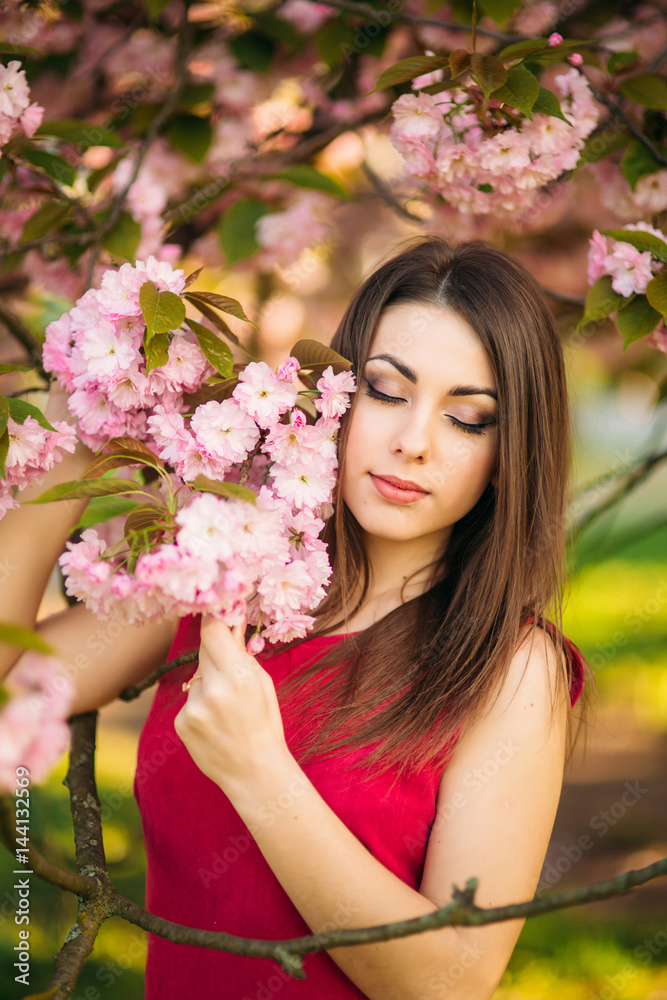 Fototapeta premium Beautiful girl posing to the photographer against the background of blooming pink trees. Spring. Sakura.