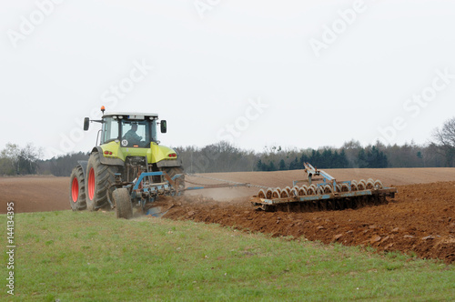 Rolnik uprawiający ziemię traktorem na polu.  photo