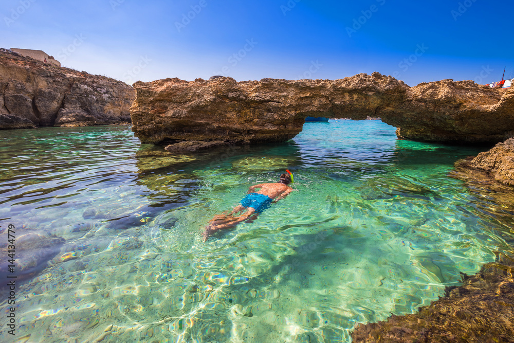 Blue Lagoon, Malta - Snorkeling tourist at the caves of the Blue Lagoon on the island of Comino on a bright sunny summer day with blue sky - obrazy, fototapety, plakaty 