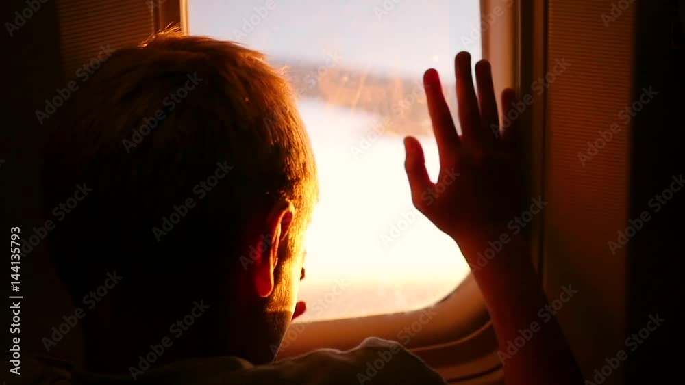 A child looking out the window of an airplane at sunset