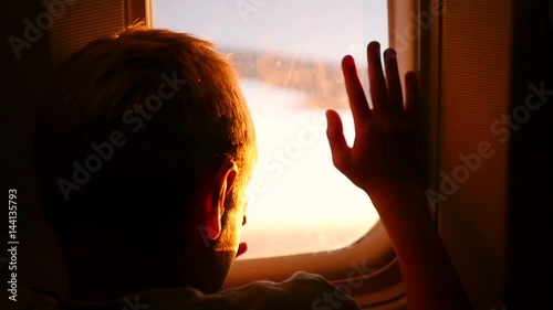 A child looking out the window of an airplane at sunset