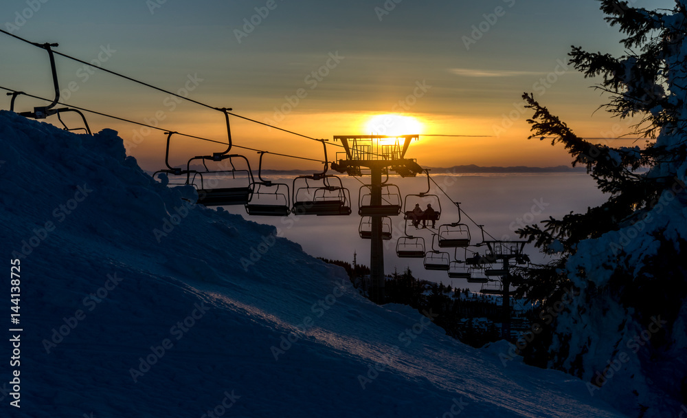 Chair ski lift with skiers at sunset Chair ski lift with skiers at sunset