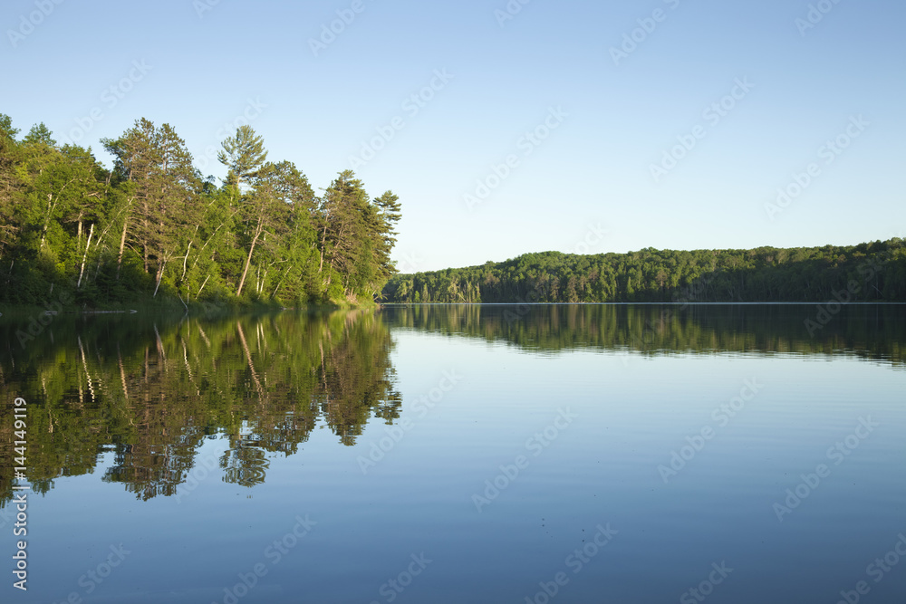 Calm northern Minnesota lake with pine trees at sunset on a clear day Calm northern Minnesota lake with pine trees at sunset on a clear day