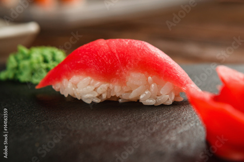 Close up view of delicious and tasty one sushi nigiri with fresh tuna fillet, served on black slate with ginger and wasabi. Japanese cuisine, healthy seafood.