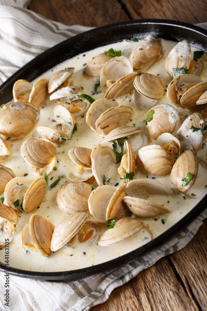 Stewed clams in creamy sauce with herbs close-up. Vertical