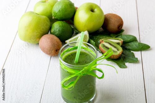 Green smoothie near ingredients for it on white wooden background. Apple, lime, spinach. Detox. Healthy drink.