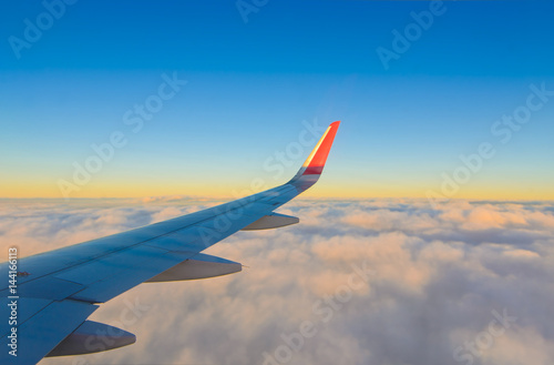 Airplane wing flying over smooth clouds and blue sky in the morning of golden time, view looking from window of aircraft