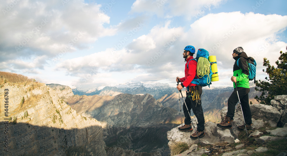 Fototapeta premium Young mountaineers standing with backpack on top of a mountain and enjoying the view