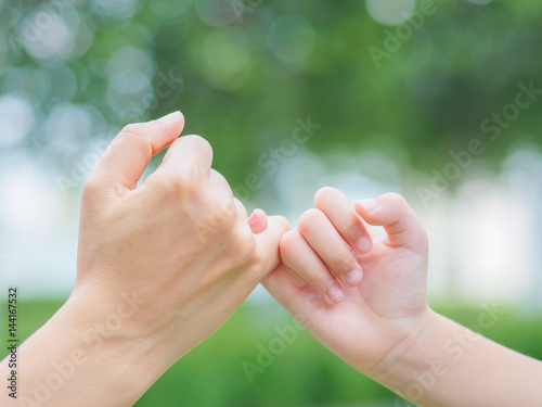 Mother holding a hand of her kid in spring day outdoors with green field background © Siam