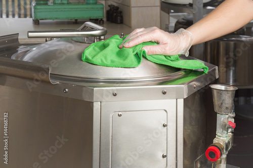 Hand in protective glove with rag cleaning kitchen equipment in the professional kitchen. Stainless steel surface. Early spring cleaning or regular clean up.