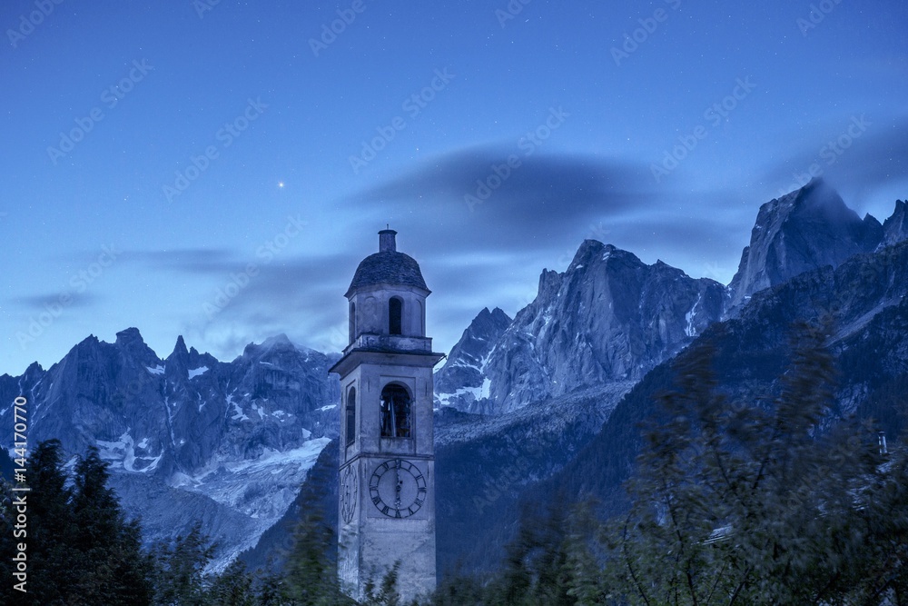Dusk in Soglio, with an amazing view on the bell tower of the village and on the granitic peaks of Pizzo Badile and Pizzo Cengalo. Val Bregaglia, Canton of Graubunden, Switzerland Europe. Dusk in Soglio, with an amazing view on the bell tower of the village and on the granitic peaks of Pizzo Badile and Pizzo Cengalo. Val Bregaglia, Canton of Graubunden, Switzerland Europe.