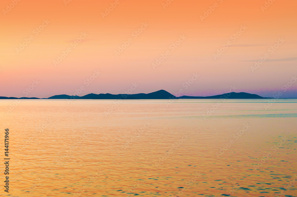 Hill range in the sea near the coast of Croatia. Sunset landscape in orange and yellow colors