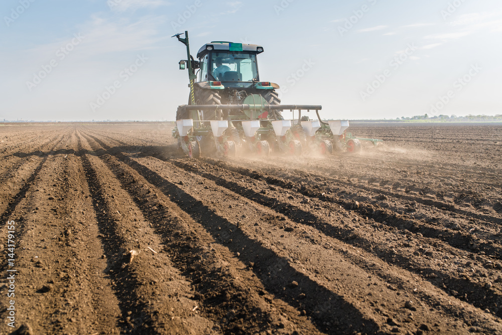 Fototapeta premium Farmer with tractor seeding - sowing soy crops at agricultural field in spring