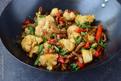 Sweet and sour beef stir fried in the wok with cauliflower and vegetables on a grey abstract background. Oriental dish. Healthy eating concept