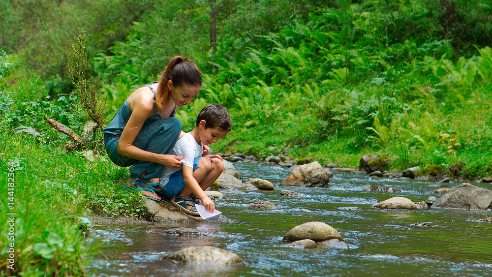 Mother with her son are launching the paper boat on a water Mother with her son are launching the paper boat on a water