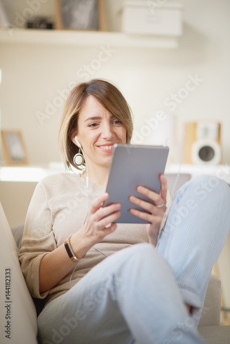 Young Caucasian woman using tablet computer and sitting on sofa at personal work space