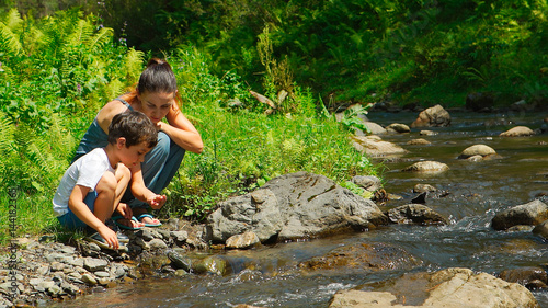 Mother with her son are sitting near a stream