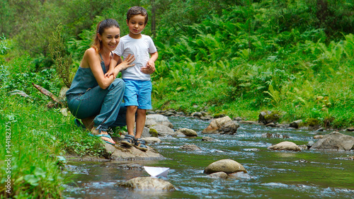 Foto Mother with her son look at the toy paper boat on a stream