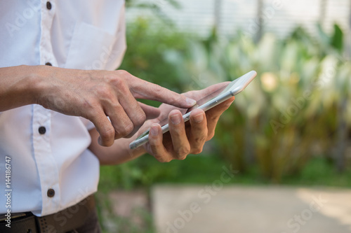 mobile concept.Business man hands holding touch screen smartphone outside in the park © Songsak C