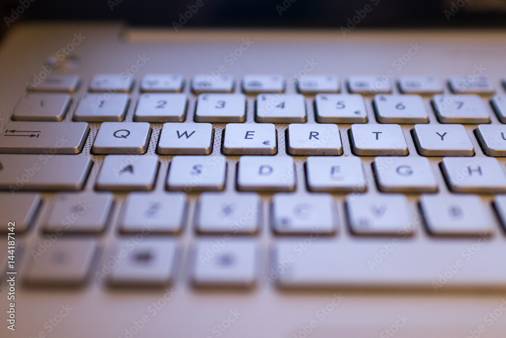 A qwerty keyboard focused on QWERTY keys. Monitor light illuminate keyboards keys