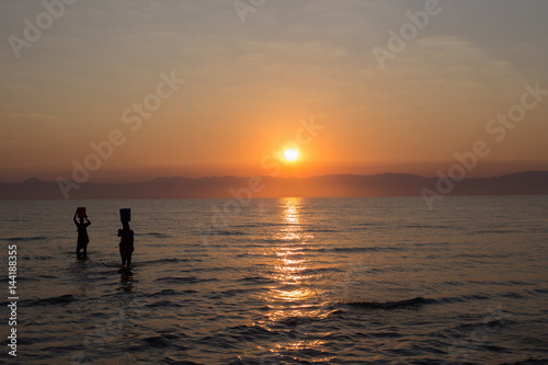 African women wade into Lake Malawi at sunrise to fill buckets for washing © Avanell