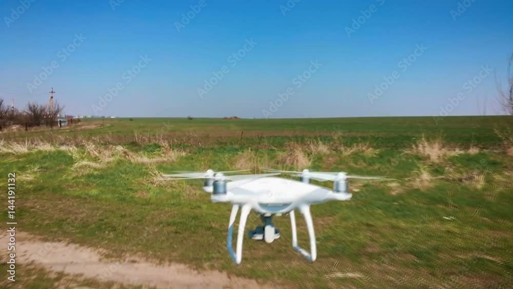 Quadrocopter flies forward over the green field in slow motion (90fps). Drone close-up, against the blue sky, the sea and cargo ships.