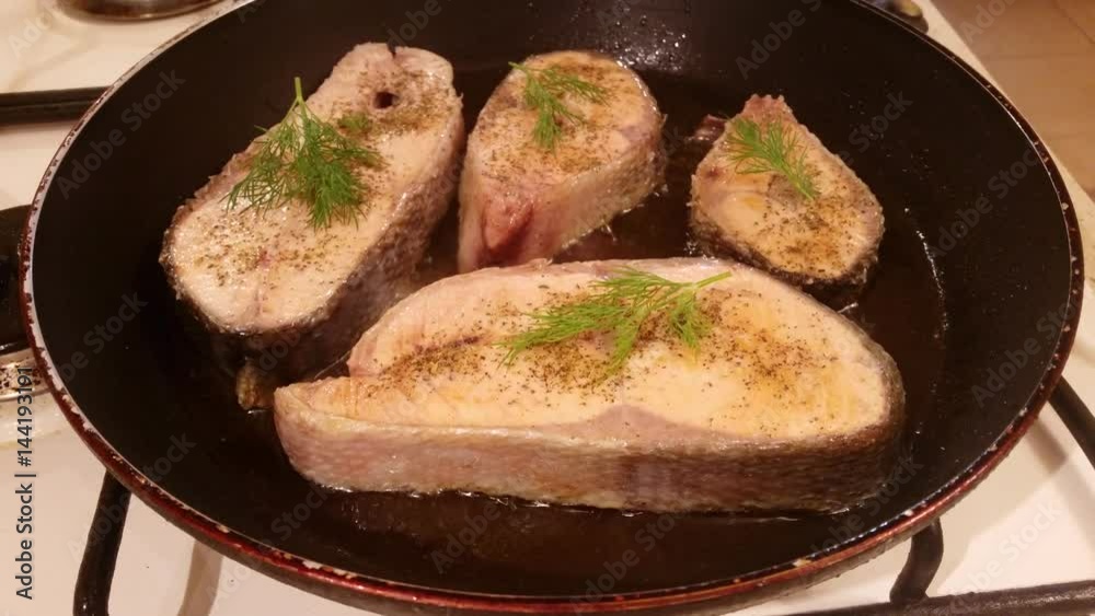 A steak of delicious fish varieties is fried in a frying pan on a kitchen gas stove A steak of delicious fish varieties is fried in a frying pan on a kitchen gas stove