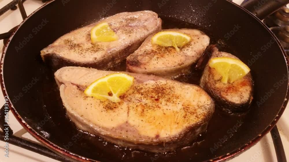 A steak of delicious fish varieties is fried in a frying pan on a kitchen gas stove A steak of delicious fish varieties is fried in a frying pan on a kitchen gas stove