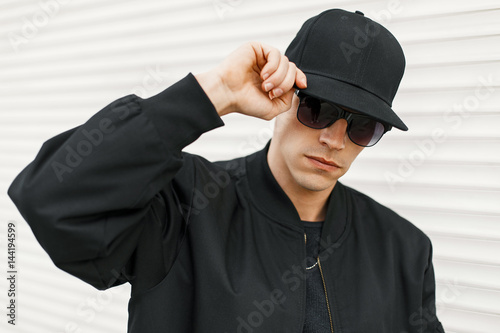 Photography Handsome man with black fashionable glasses and a black baseball cap posing near