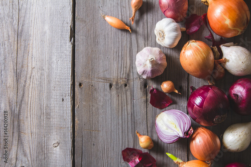 Several kinds of different onion bulbs lying on an old wooden table.