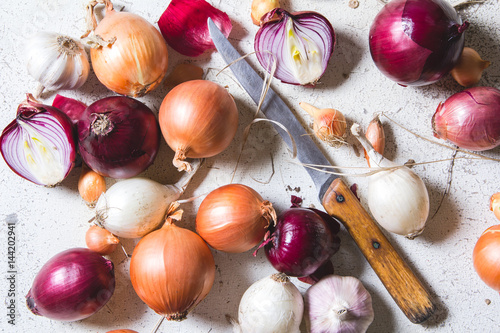 Several kinds of different onion bulbs lying on an old wooden table painted in white.