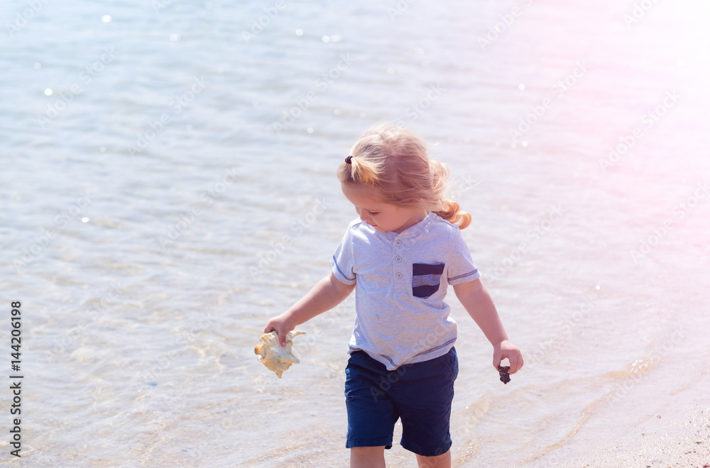 happy cute baby boy smiling with marine shell in hand happy cute baby boy smiling with marine shell in hand
