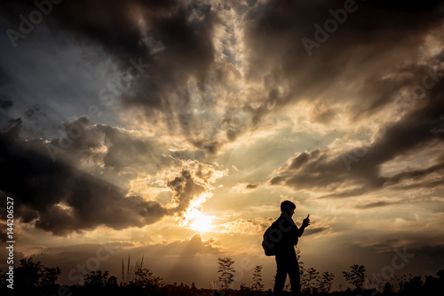 Silhouette man with backpack use smartphone in hands at sunset background  Travel concept.