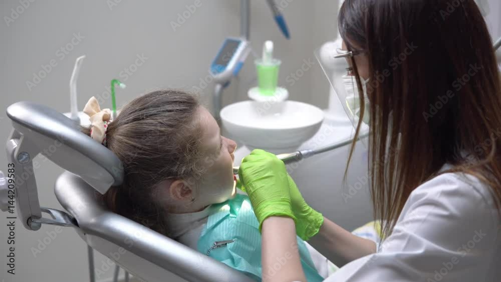 Female dentist drilling tooth of cute little girl at the dentist cabinet and uses saliva ejector. Shot in 4k Female dentist drilling tooth of cute little girl at the dentist cabinet and uses saliva ejector. Shot in 4k