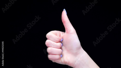 Female hand showing thumbs up gesture over black background photo