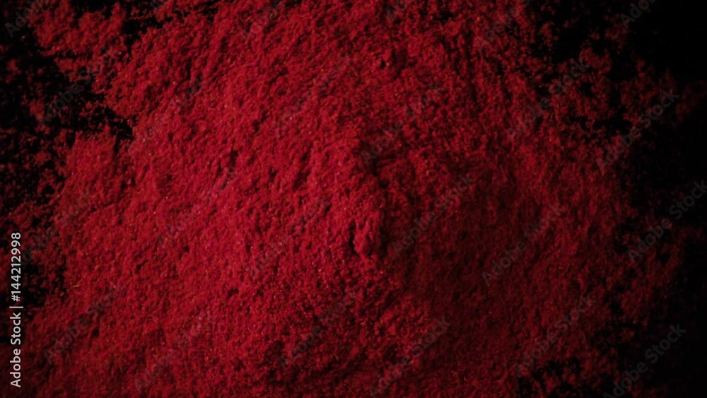 A large amount of paprika red powder drops down on the black table. Slow motion, top view