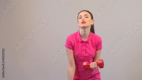 Attractive young woman in sports clothing, fitness and training biceps with dumbbells