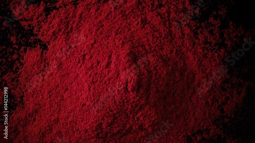 A large amount of paprika red powder drops down on the black table. Slow motion, top view