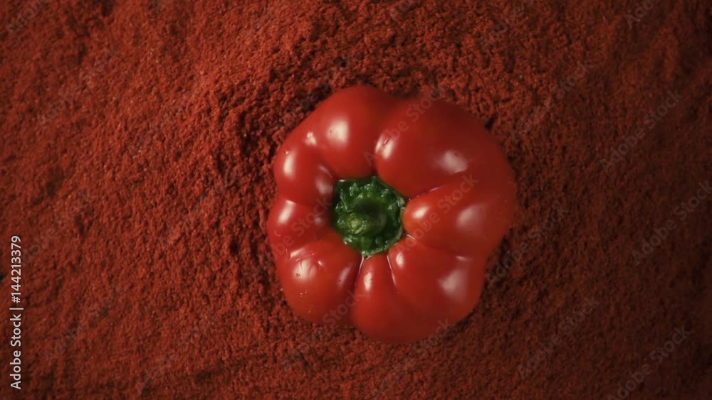Large wet red paprika pepper drops down on the pepper powder paprika on a black table, slow motion, top view