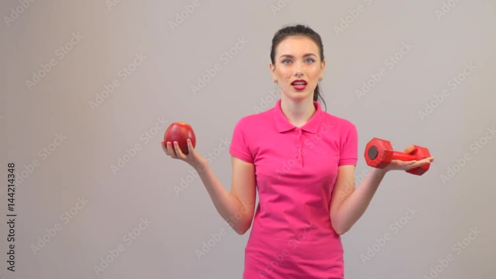 Elements of a healthy lifestyle. Attractive young woman possing with apple and dumbbell Elements of a healthy lifestyle. Attractive young woman possing with apple and dumbbell