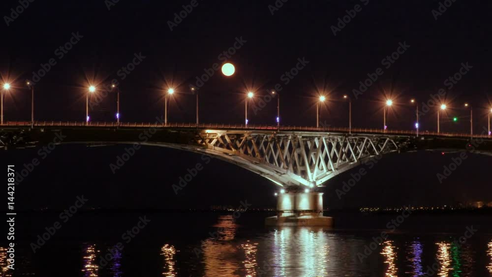 Full moon rises over the bridge. Time-lapse. Road bridge between the cities of Saratov and Engels, Russia. The Volga River. The evening lights of cars and street lights. 4K, Ultra HD Full moon rises over the bridge. Time-lapse. Road bridge between the cities of Saratov and Engels, Russia. The Volga River. The evening lights of cars and street lights. 4K, Ultra HD